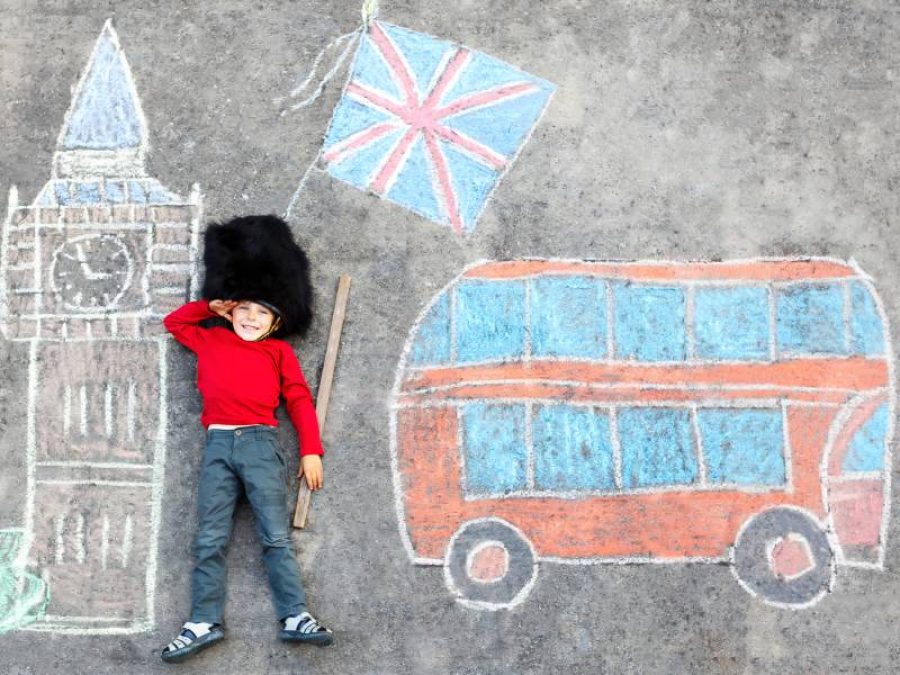 Happy little kid boy in british queen's guard soldier uniform having fun with London picture drawing with colorful chalks. With Big Ben, Union Jack and red bus as british doodles (Happy little kid boy in british queen's guard soldier uniform having fu